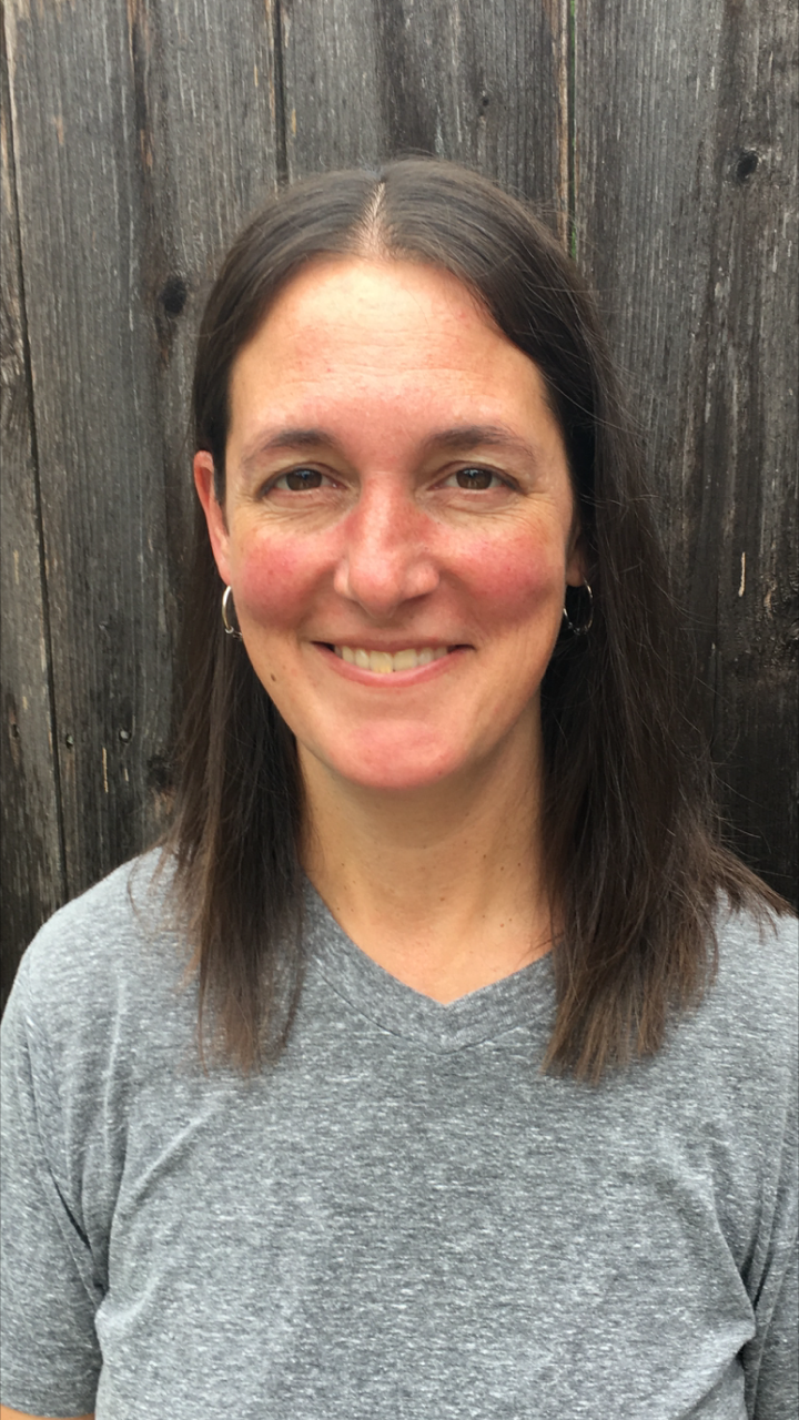 Bio photo of Sarah Byerley smiling in a gray in front of a wooden wall